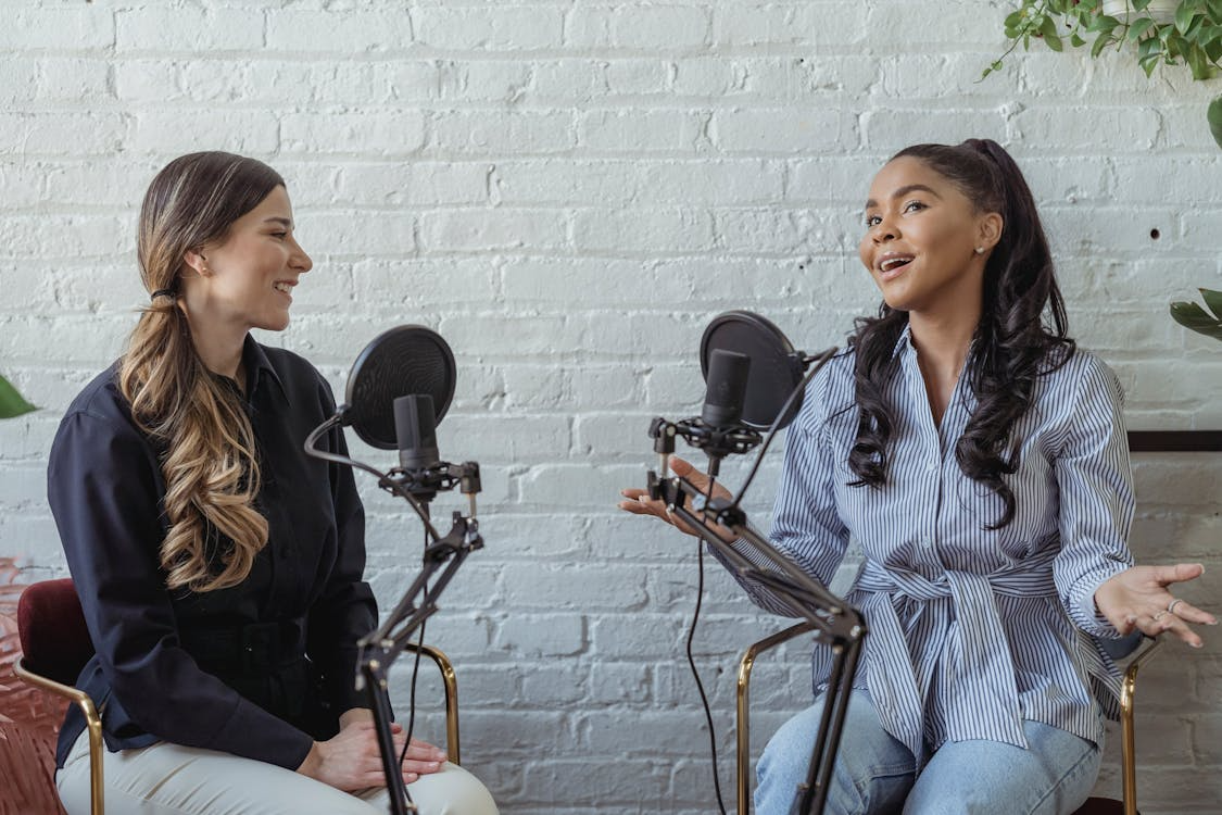 Two women recording a conversational podcast with microphones