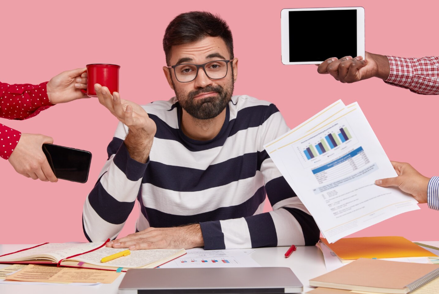 Overwhelmed office worker because of multitasking surrounded by phone, tablet, and papers