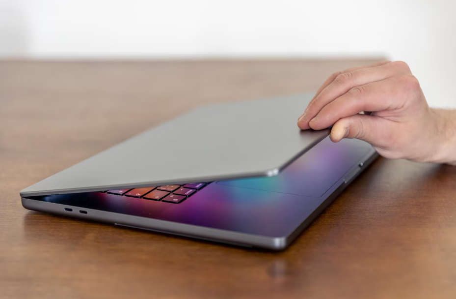 Hand closing a laptop on a wooden desk, signaling a digital break